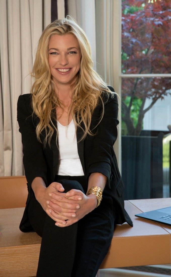 Nicole Junkerman smiling warmly, seated at a sunlit desk while reading
